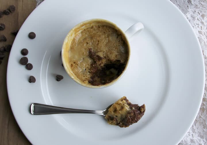 Spoonful of cookie in a mug on a plate with the mug.