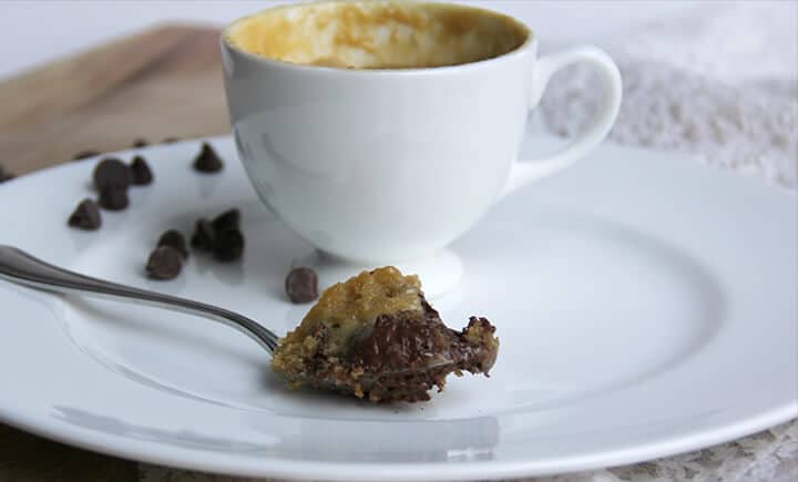 A spoonful of chocolate chip cookie in a mug on a plate next to the cup.