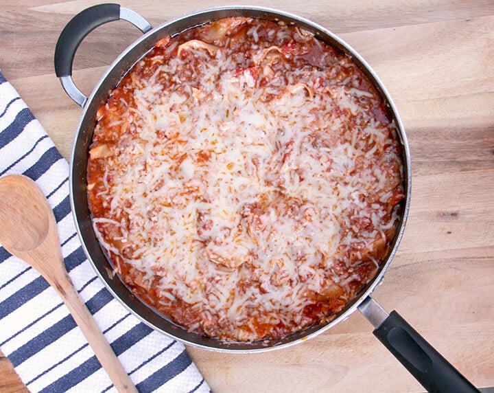 A skillet with cheesy lasagna with a wooden spoon next to it for a romantic dinner at home.