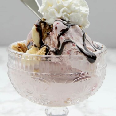 Strawberry ice cream topped with whipped cream and hot fudge sauce in a glass bowl for a perfect romantic dinner at home.