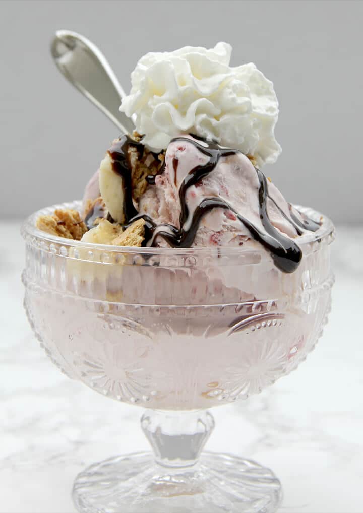 Strawberry ice cream topped with whipped cream and hot fudge sauce in a glass bowl for a perfect romantic dinner at home.