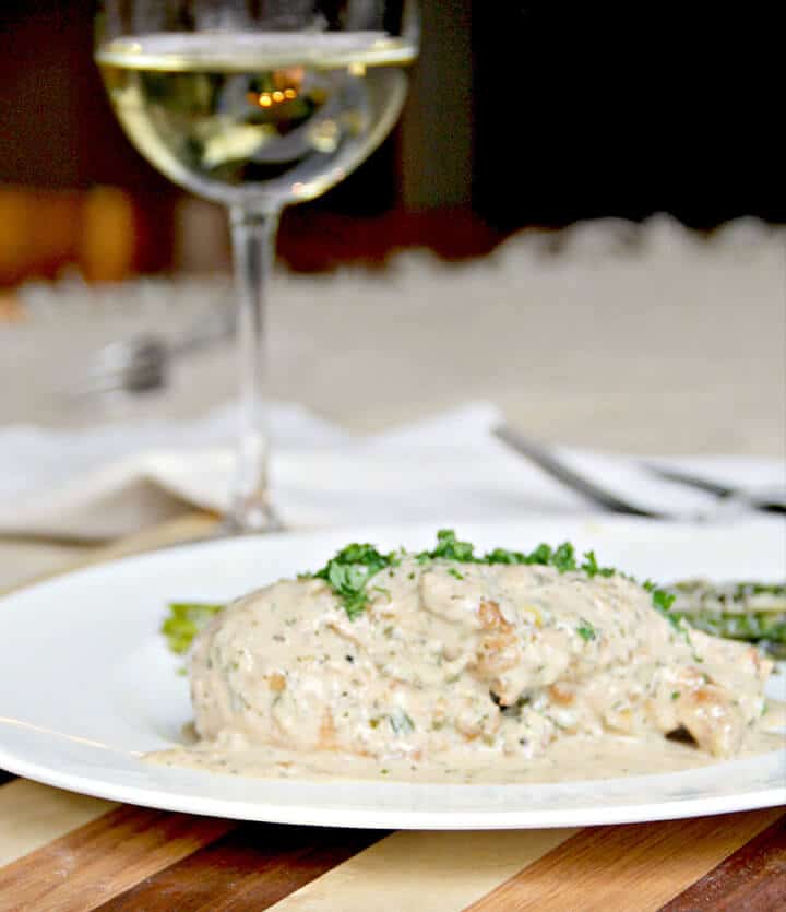 Chicken with mustard sauce on a white plate with a glass of wine in the background for a perfect romantic dinner at home.