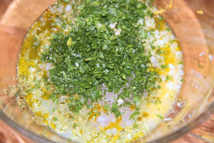 A bowl with fresh basil, lemon juice and zest, and other ingredients for the dressing for pesto pasta salad.