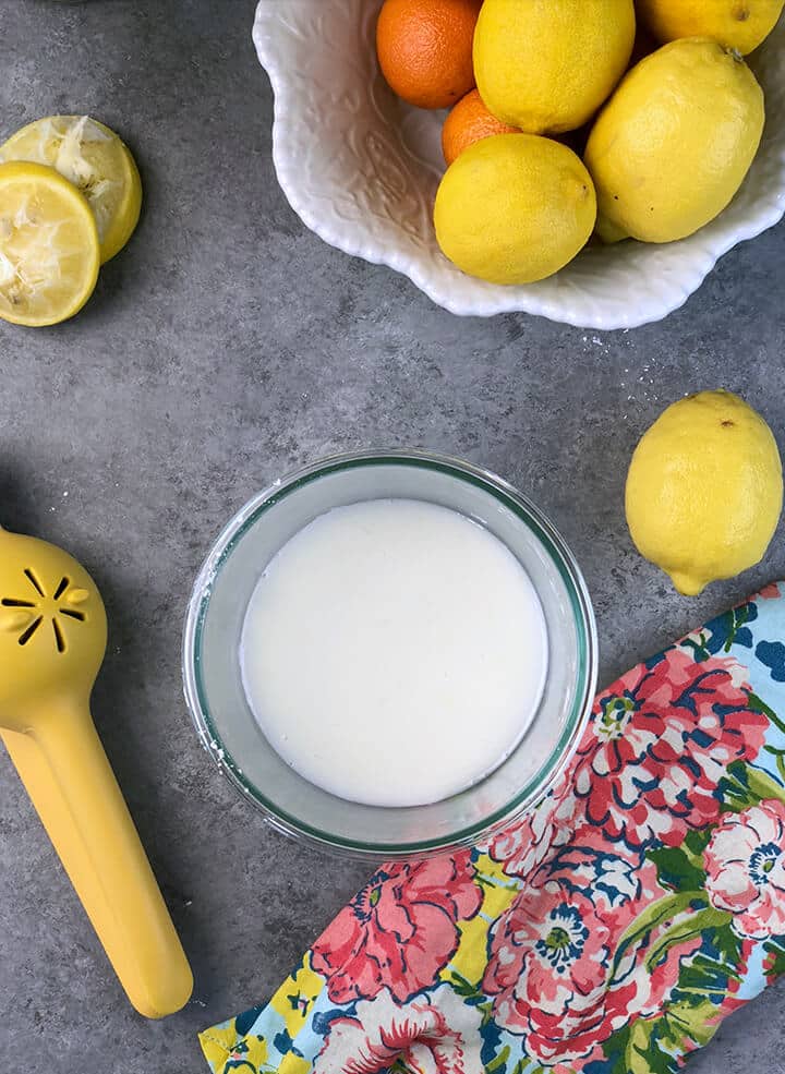 Lemon glaze in a bowl with lemons and a citrus juicer on the side.