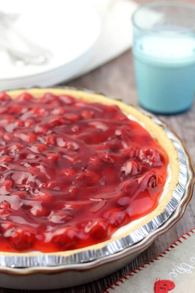 Close up side view of cherry cheese pie in a pie plate.