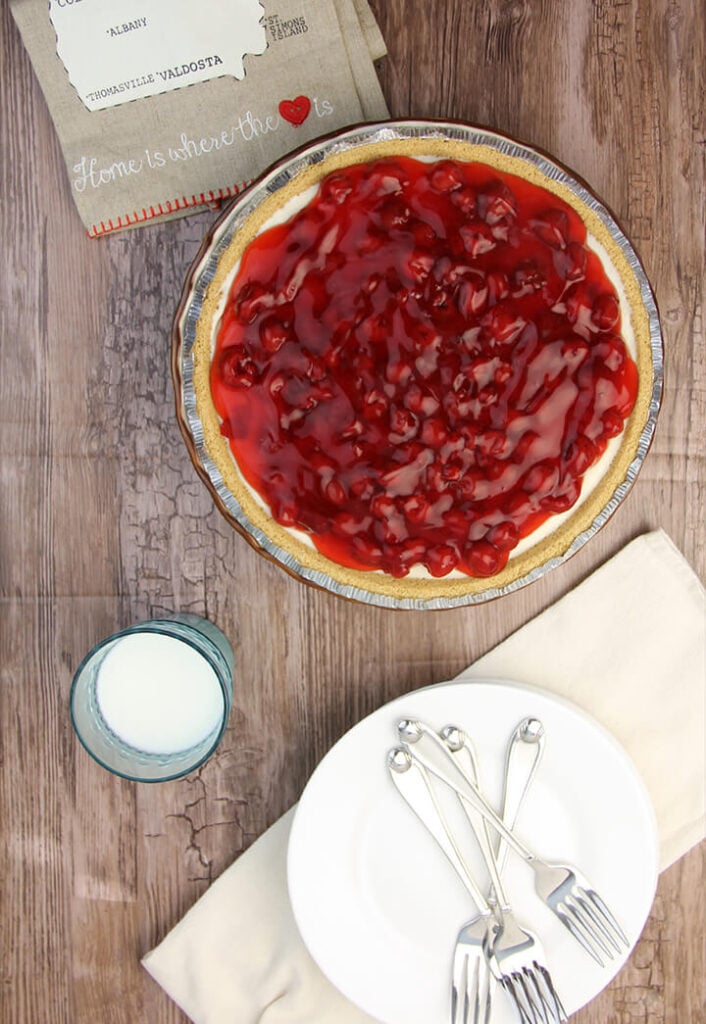 Whole cherry cream cheese pie on a board with plates and forks.