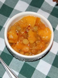 Peach chutney in a white bowl on a green checkered tablecloth.