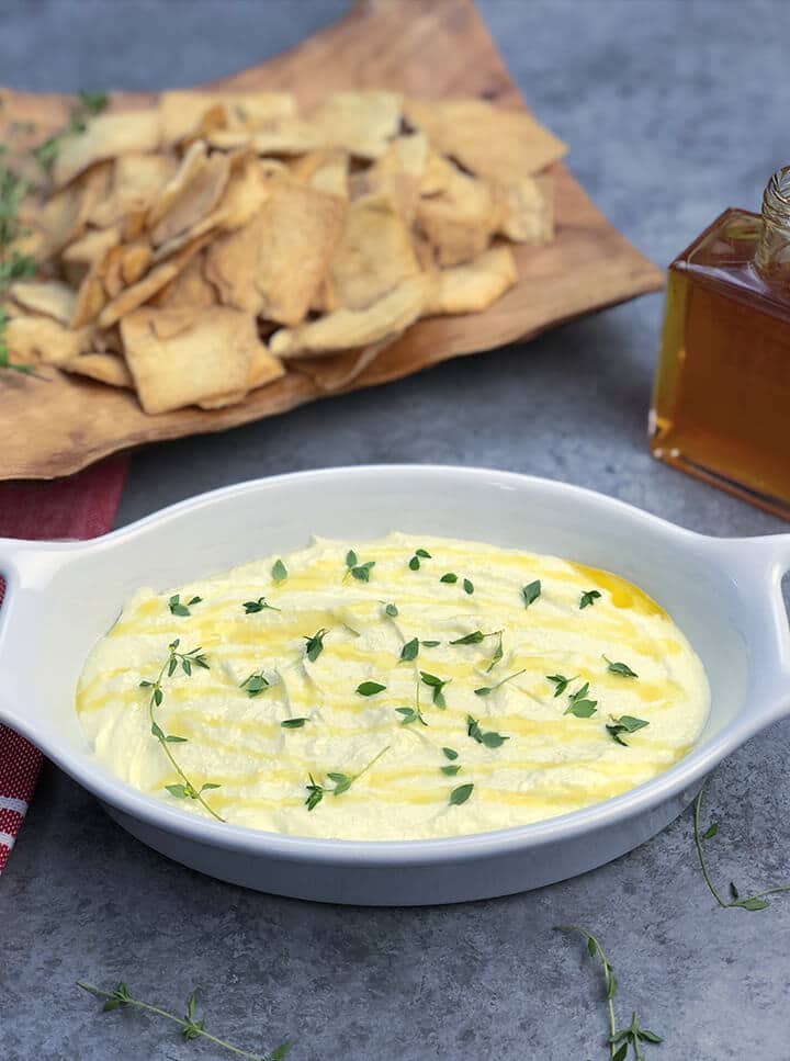 White bowl of whipped feta dip with honey and chips in the background.