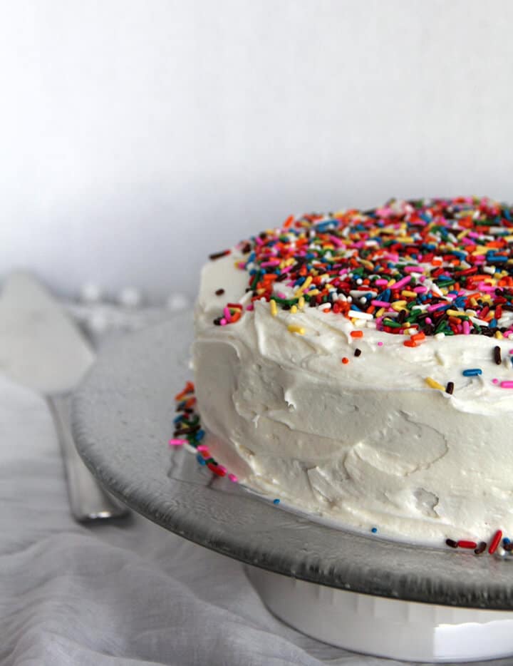 Side view of a whole sprinkle cake with easy buttercream frosting on a platter.