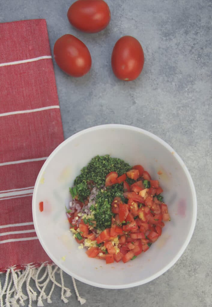 A white bowl with tomatoes and herbs chopped up to make homemade bruschetta.