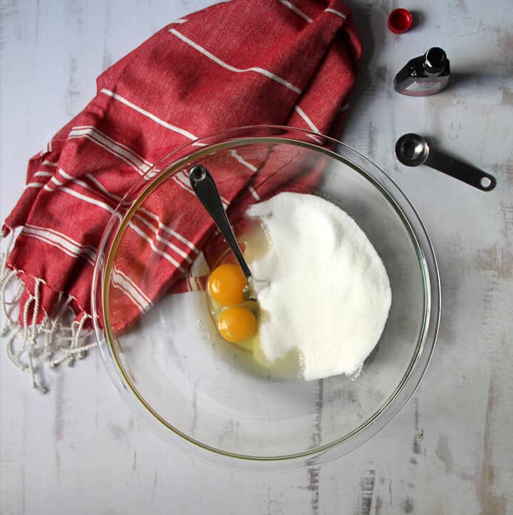 A bowl of eggs and sugar beside a red towel.