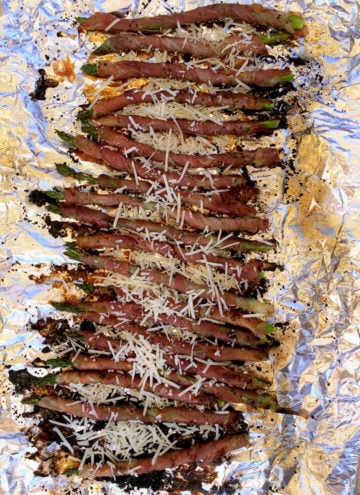 A foil covered tray of prosciutto wrapped asparagus with parmesan.