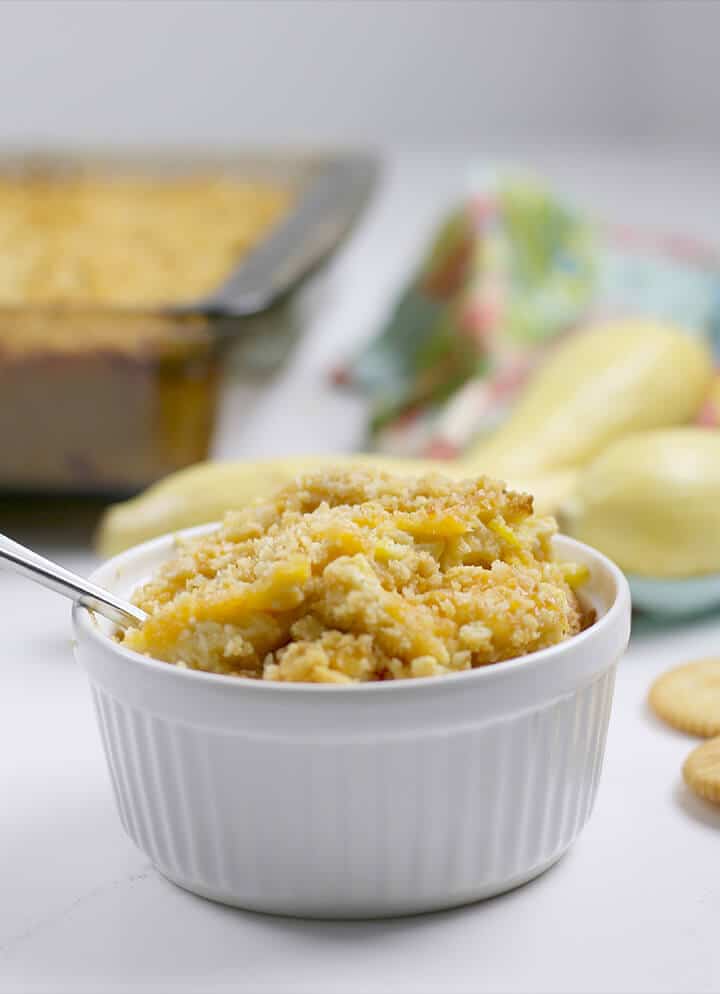 A serving of easy squash casserole with the full dish in the background.