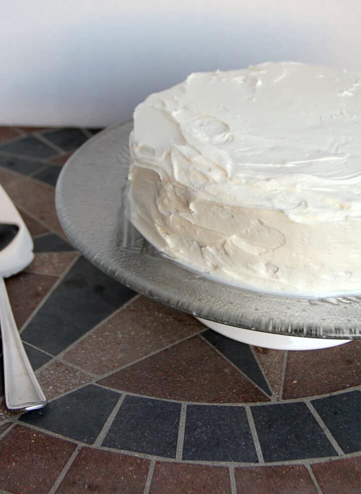 A cake on a glass platter frosted with easy buttercream frosting.