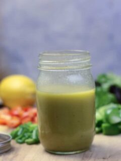 A jar of French salad dressing with lemons and peppers in the background.