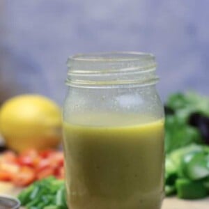 A jar of French salad dressing with lemons and peppers in the background.