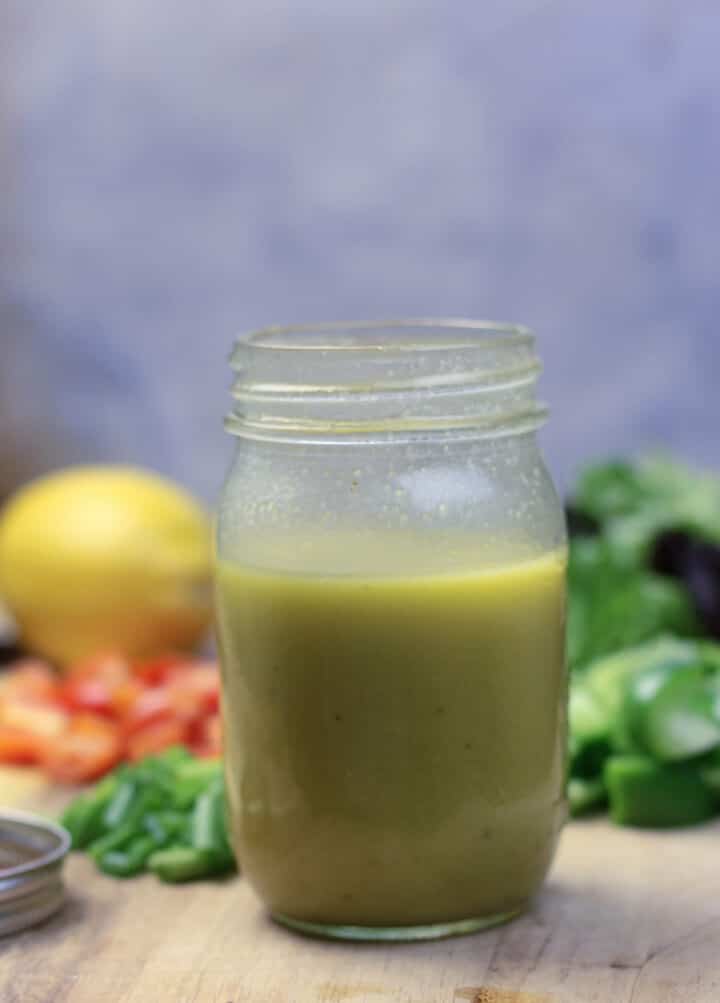 A jar of French salad dressing with lemons and peppers in the background.