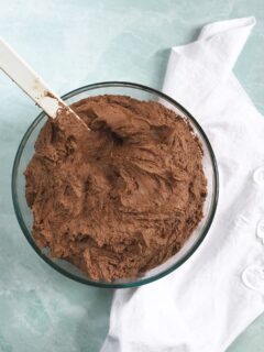 A bowl of the best chocolate buttercream frosting with a white napkin on the side.
