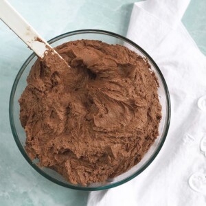 A bowl of the best chocolate buttercream frosting with a white napkin on the side.