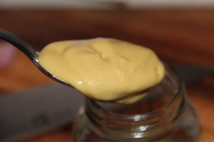 A spoon of Dijon mustard going into a jar to make French salad dressing.
