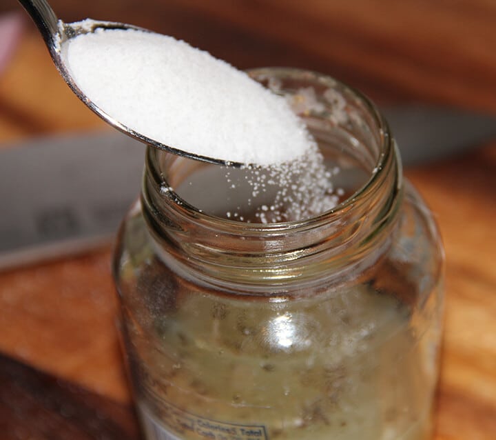Spoonful of sugar pouring into jar for lemon vinaigrette.