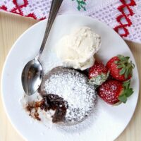 Baked chocolate lave cake on a white plate with ice cream and strawberries.