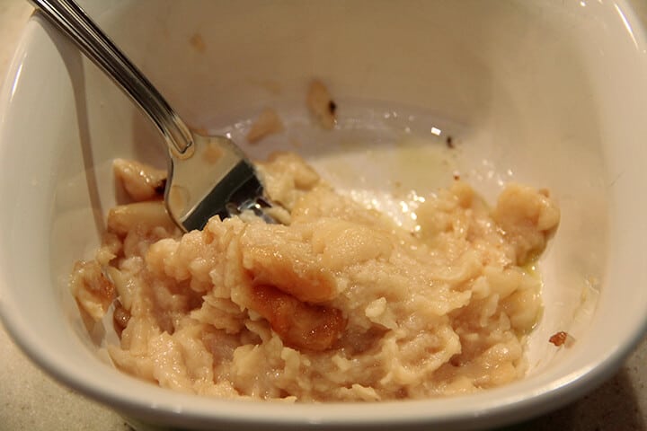 A bowl of mashed roasted garlic with a fork on the side.