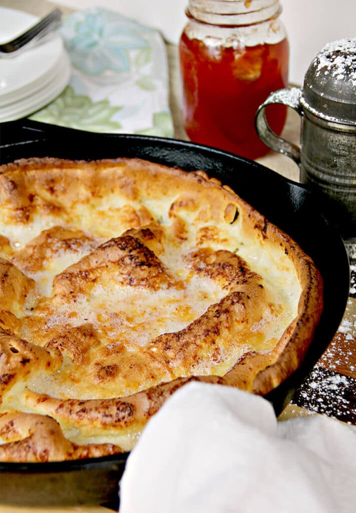 Dutch baby german pancake in a cast iron skillet with a jelly jar in the background.