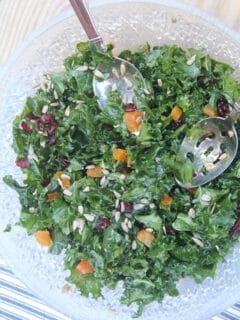 Easy kale salad in a bowl with salad tongs over a blue and white towel.