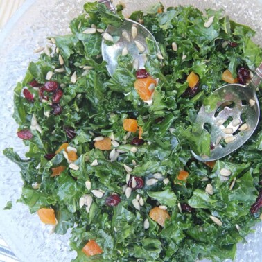 Easy kale salad in a bowl with salad tongs over a blue and white towel.