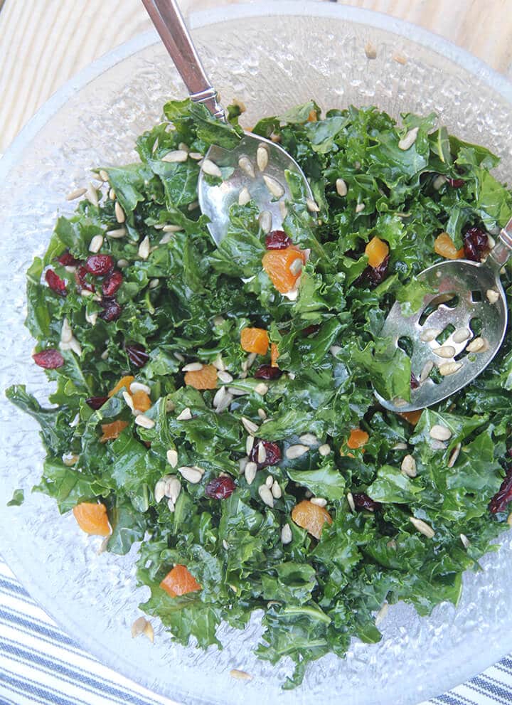 Easy kale salad in a bowl with salad tongs over a blue and white towel.