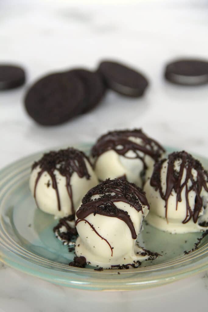 Four white chocolate covered Oreo truffles on a blue plate.