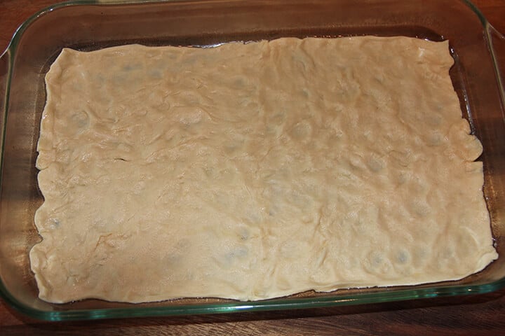 Crescent rolls spread out to bake crust for sausage breakfast pizza.