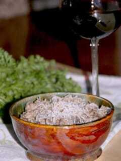 A bowl of sausage risotto with a glass of wine in the background.