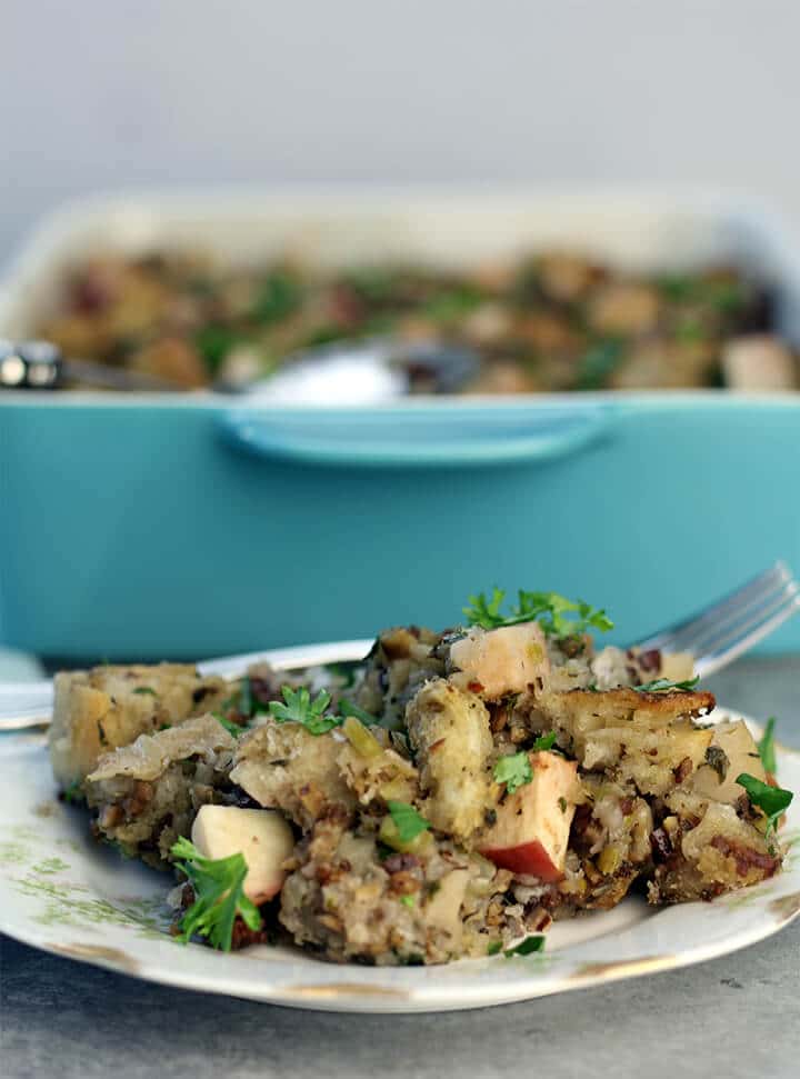 A serving of apple sausage stuffing on a plate with the dish in the background.