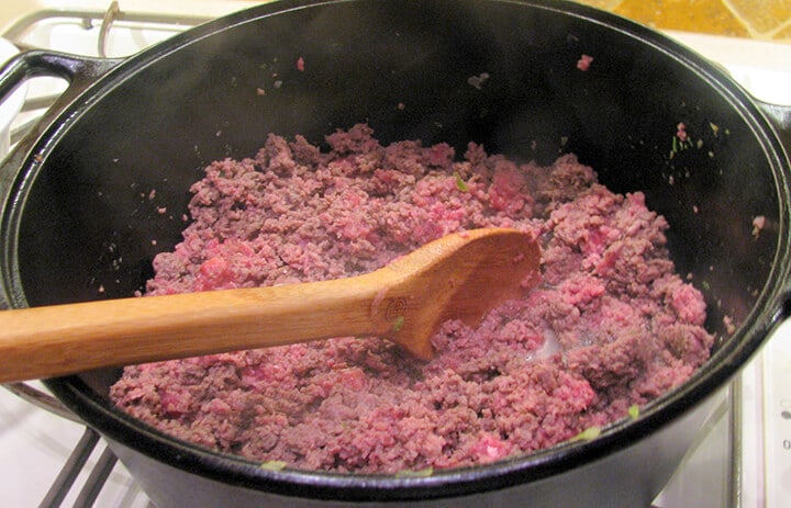 Ground beef in a pot with a wooden spoon.