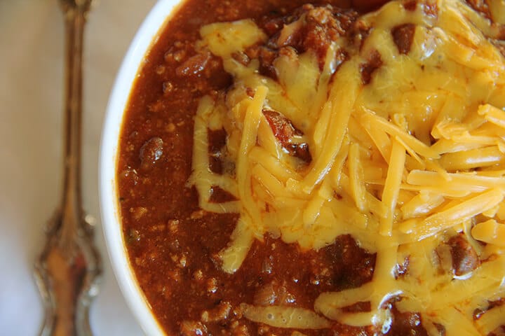 Closeup photo of a bowl of classic beef chili with grated cheese.
