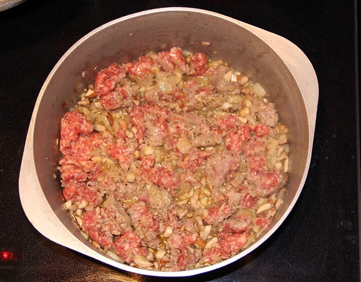 A pot with sausage, onions, and mushrooms cooking.