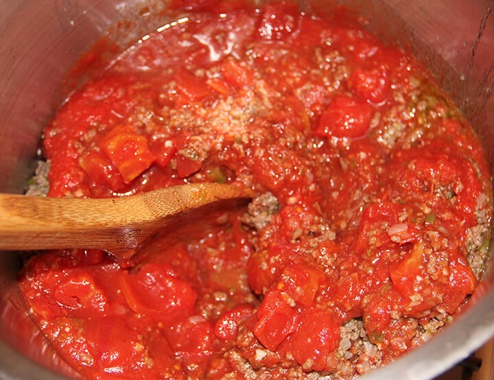 Tomatoes in a pot with ground beef and a wooden spoon.