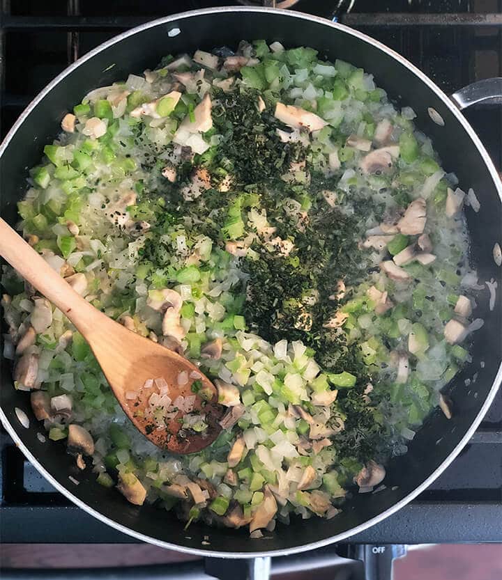 Celery, mushrooms, and onions with herbs in a skillet.