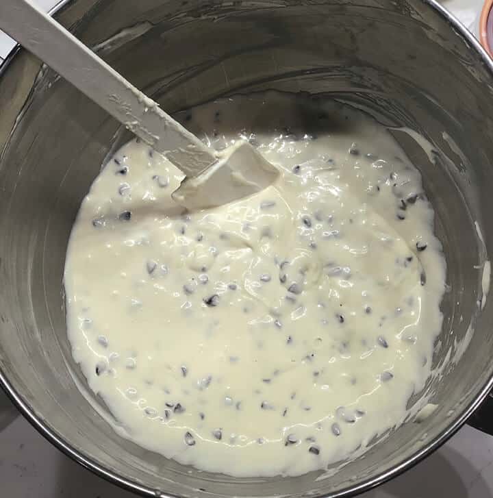Chocolate chip cheesecake batter in the mixer bowl with a white spatula.