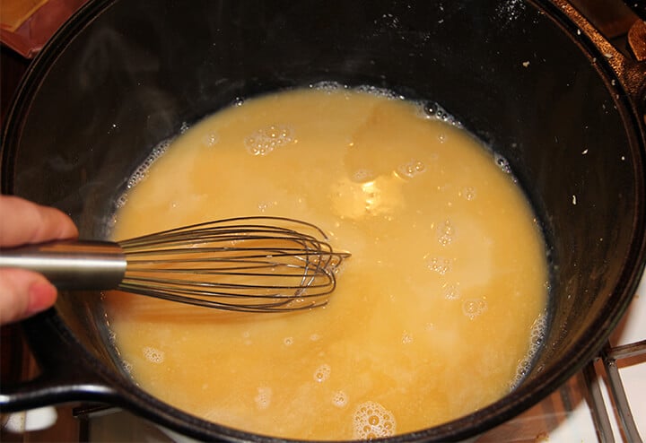 Whisking chicken broth in a large black pot.
