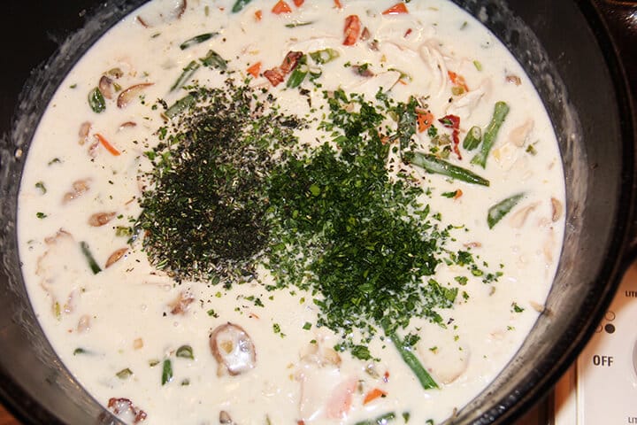 A pot of filling for chicken pot pie with herbs being stirred in.