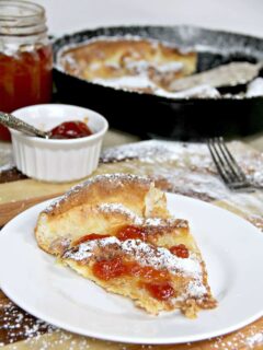 A white plate on a cutting board with a slice of Dutch Baby German Pancake.