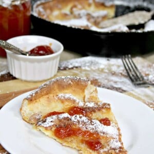 A white plate on a cutting board with a slice of Dutch Baby German Pancake.