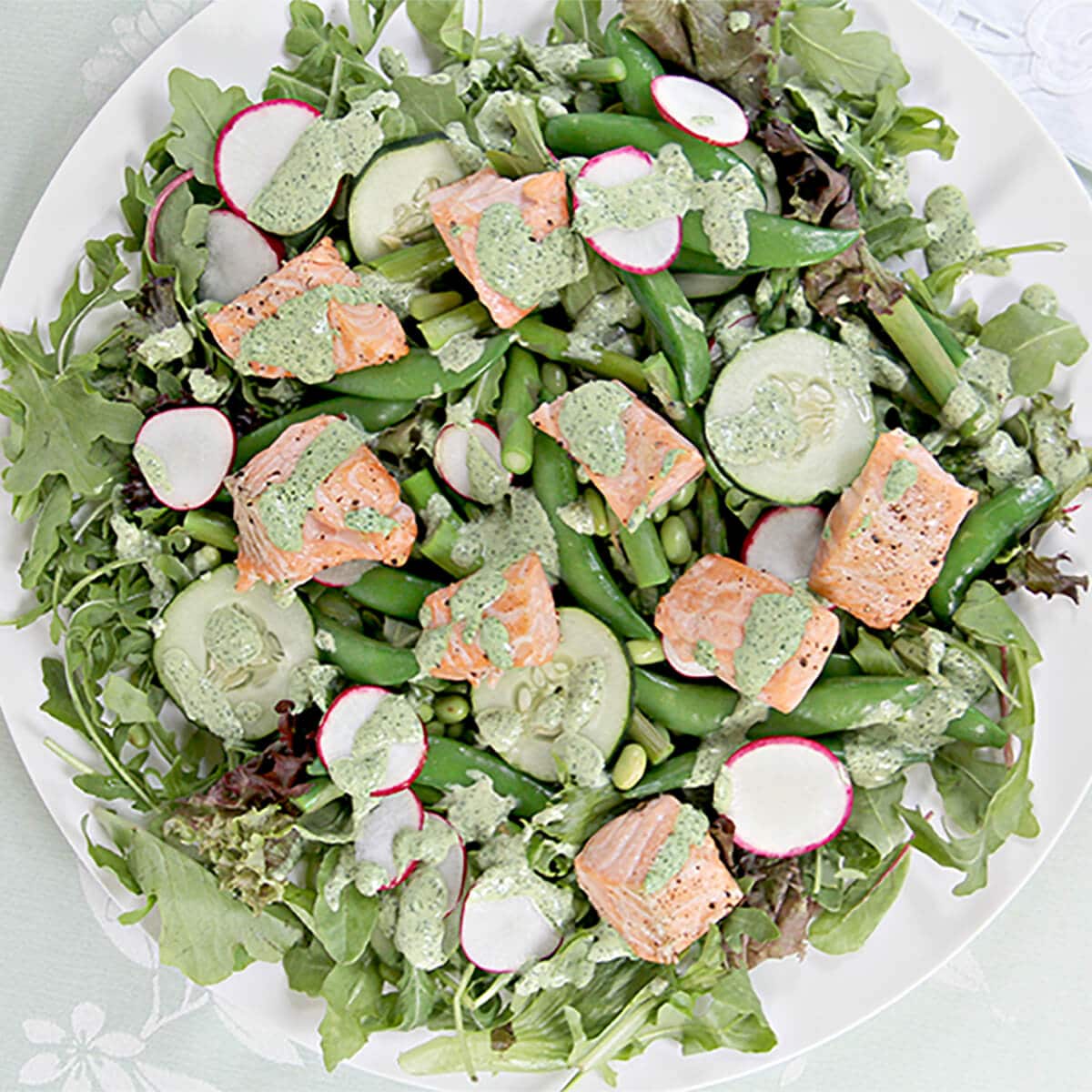 Overhead shot of spring salad with asparagus, sugar snap peas, cucumbers, salmon on a white plate.
