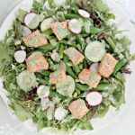 Closeup of spring salad with baked salmon and fresh spring vegetables on a white platter.