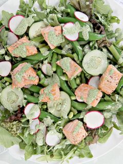 Closeup of spring salad with baked salmon and fresh spring vegetables on a white platter.