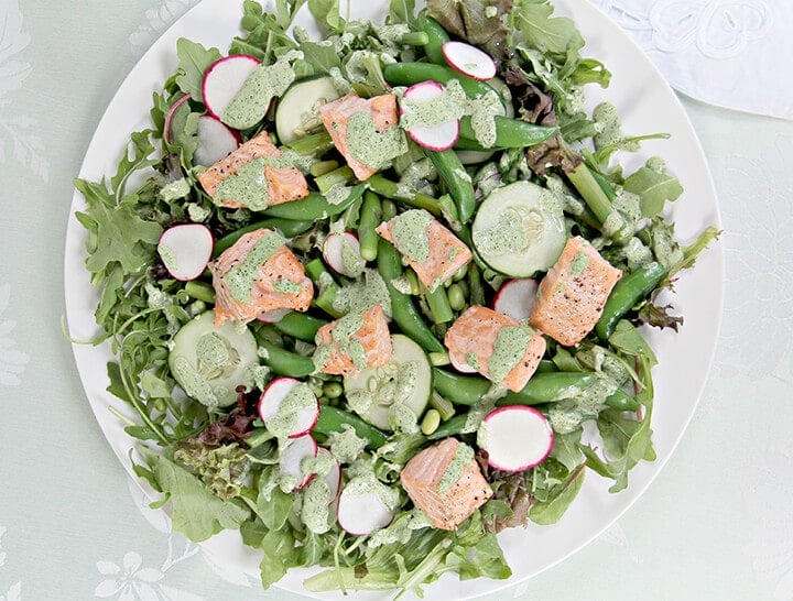 Baked salmon on top of greens with fresh spring vegetables on a white plate.