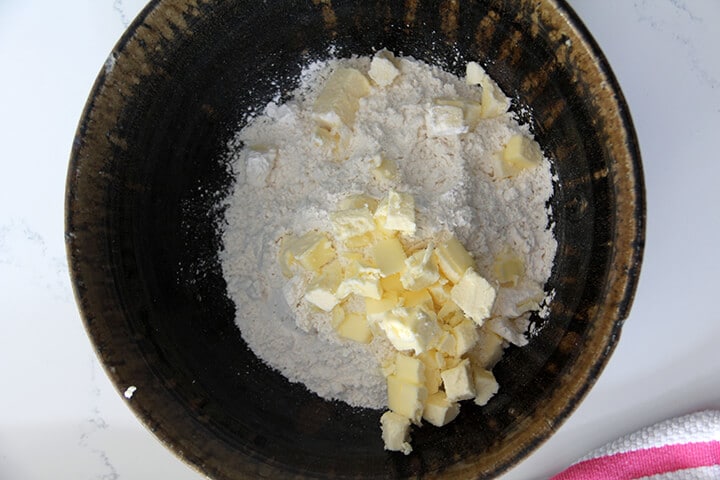 A brown bowl filled with flour and chunks of butter.